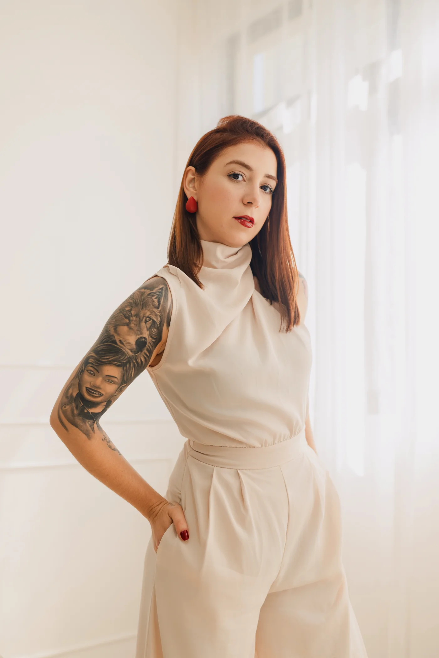 Fernanda Smanio em pé, de macacão claro, junto à cortina